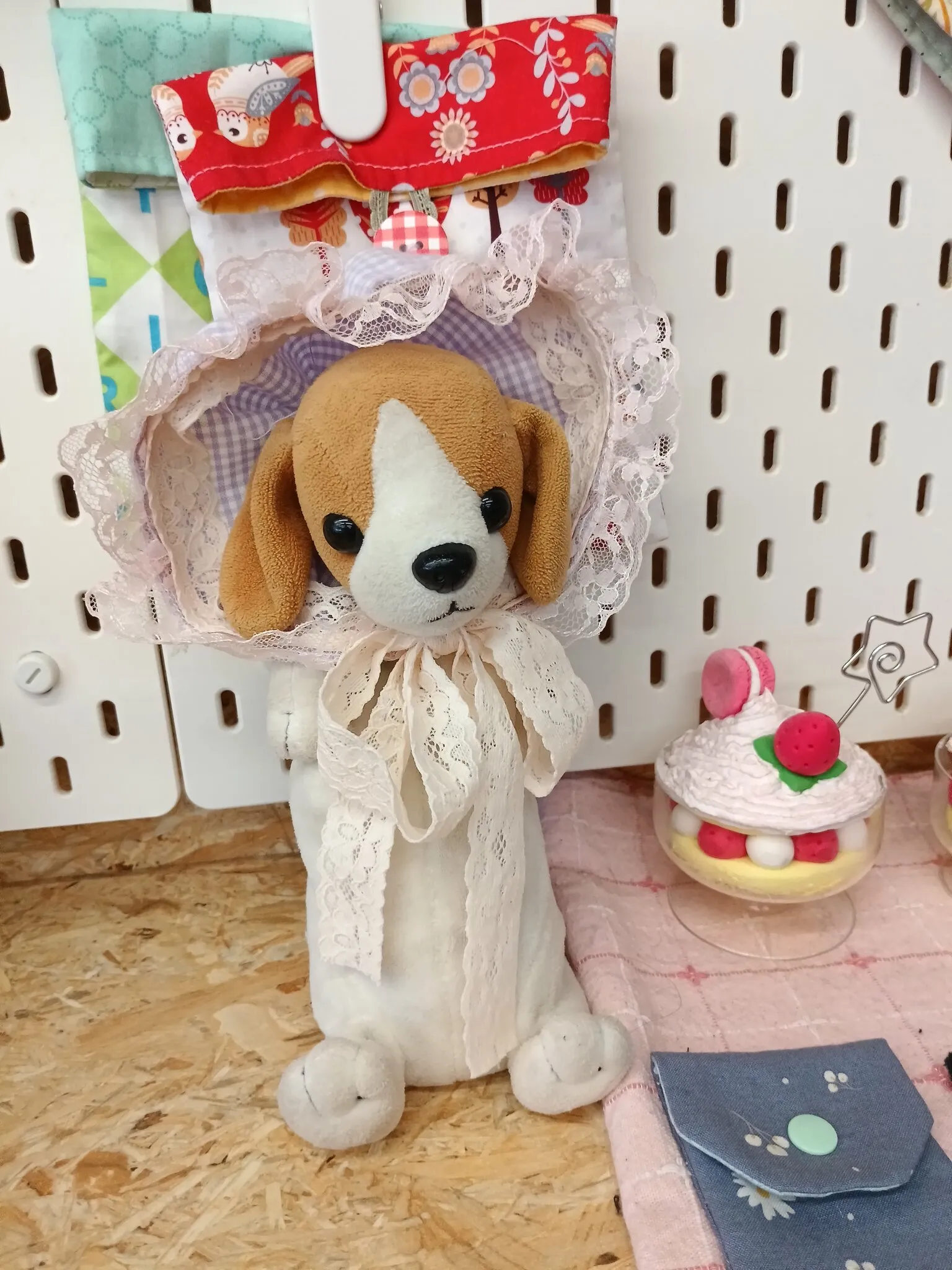 A beagle plush toy wearing the finished bonnet: lavender gingham with a pale pink lace ruffle around the face, tied under the chin with a wide lace bow.